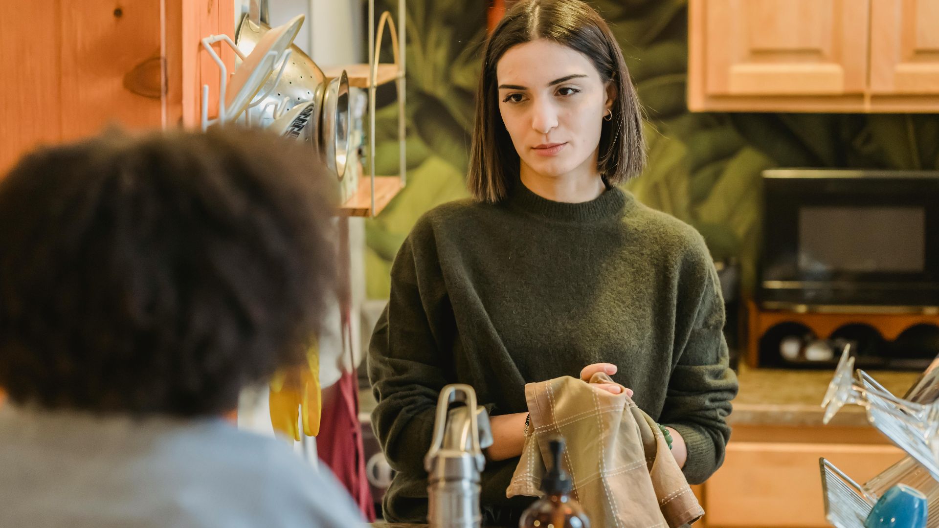 Content young best friends gathering and speaking with each other in contemporary kitchen with utensil