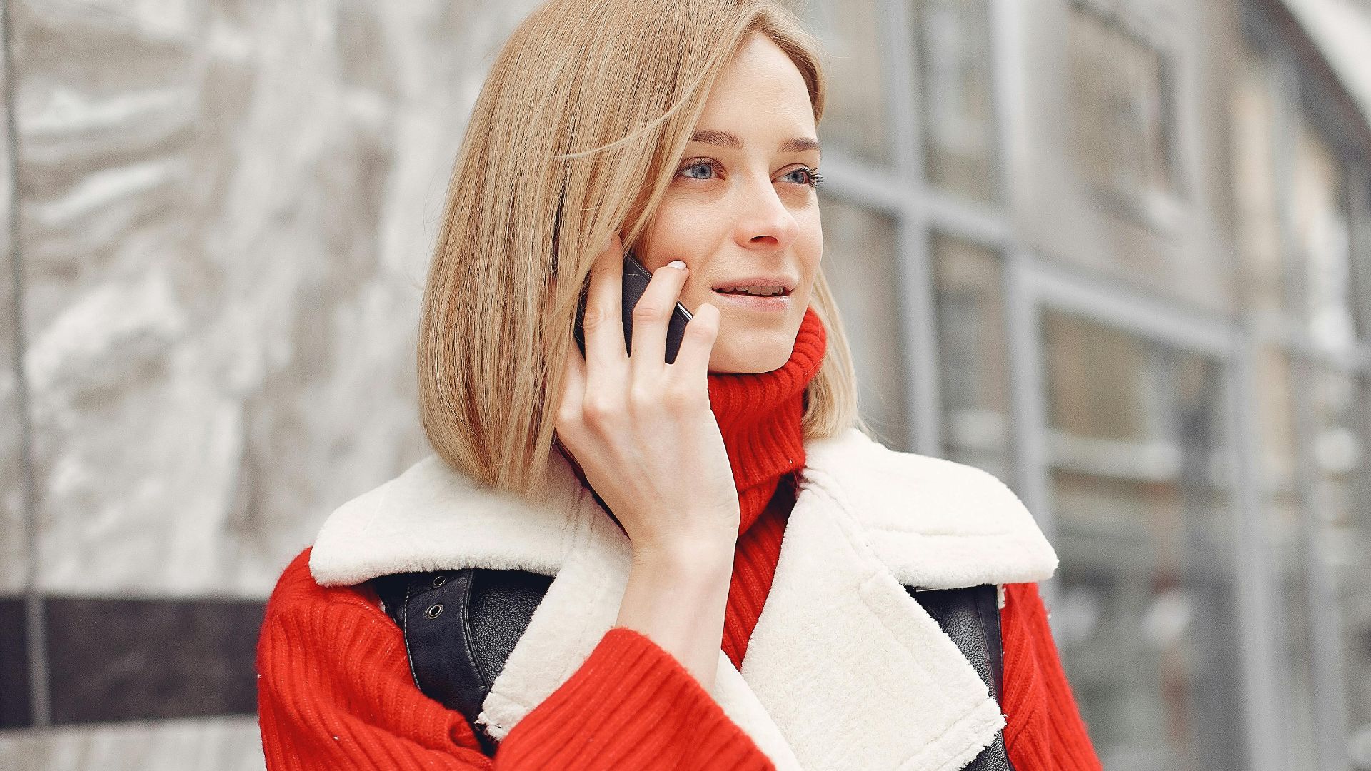 Woman in a vibrant red sweater and black vest talking on the phone outdoors.
