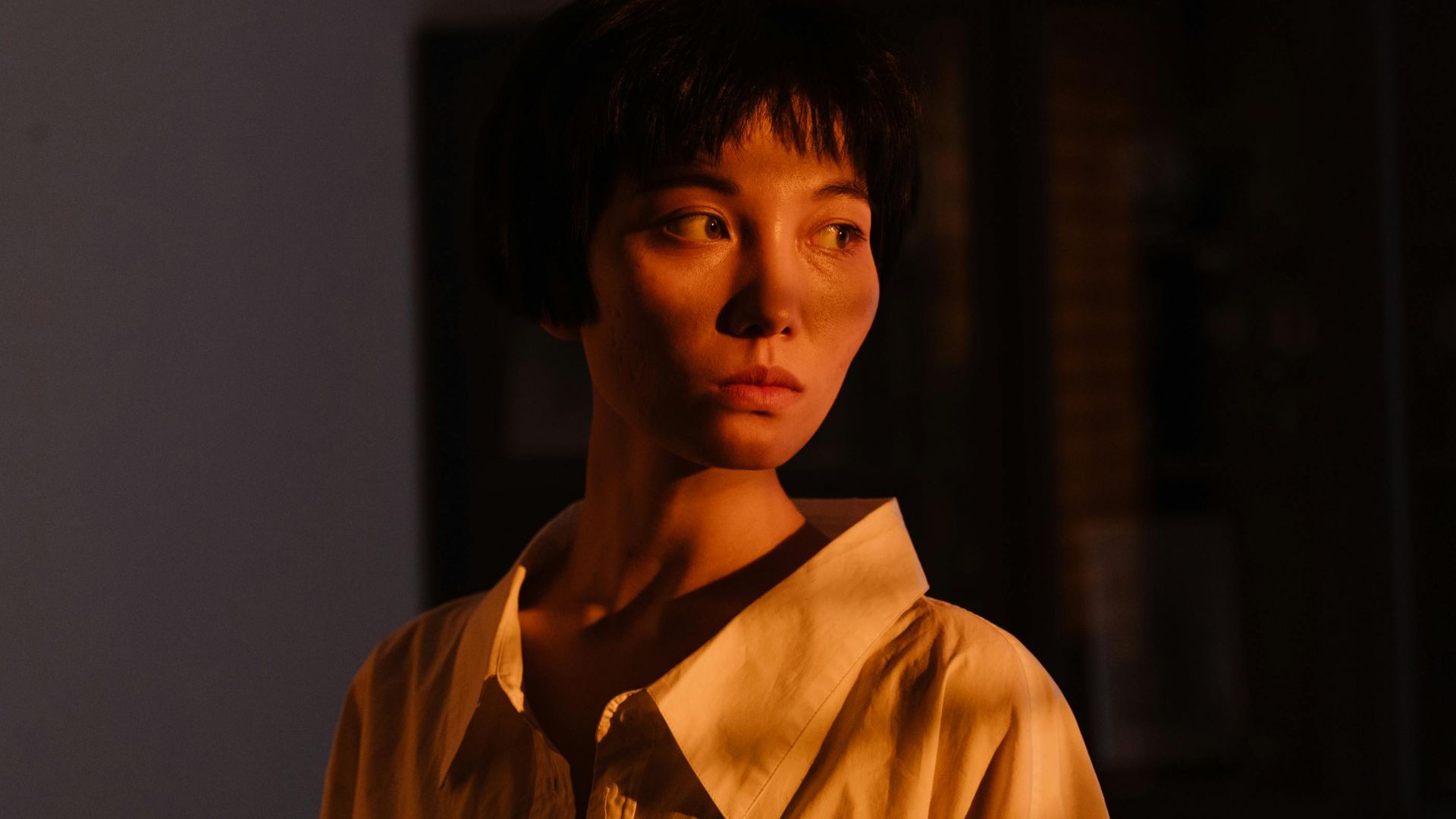 Portrait of an Asian woman looking sideways, illuminated by warm light and shadows.