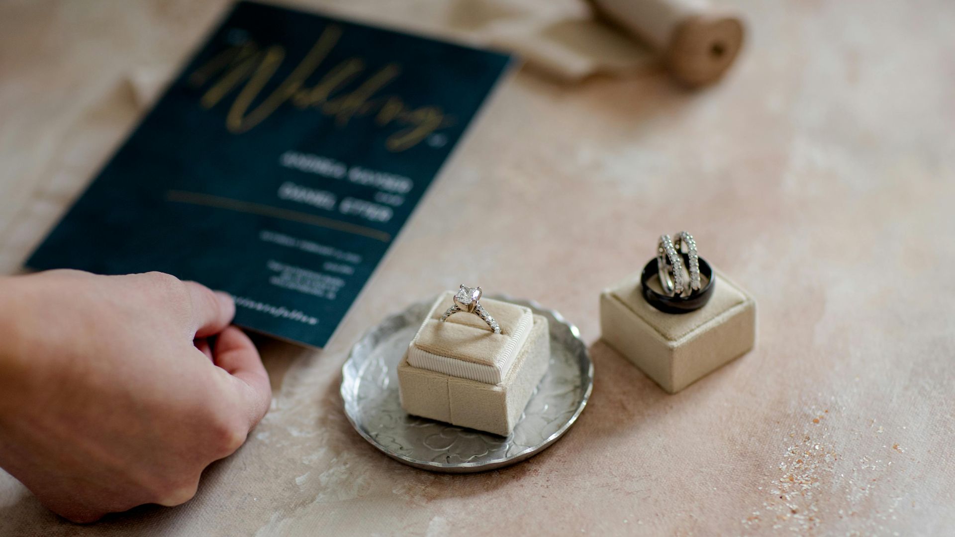 Close-up of wedding invitation and diamond rings on a tray, showcasing elegance and preparation.