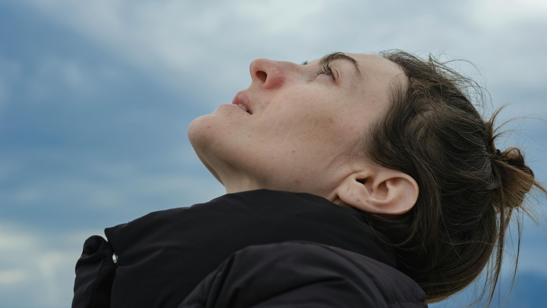 Close-up side profile of a woman gazing upwards against a blue sky backdrop.