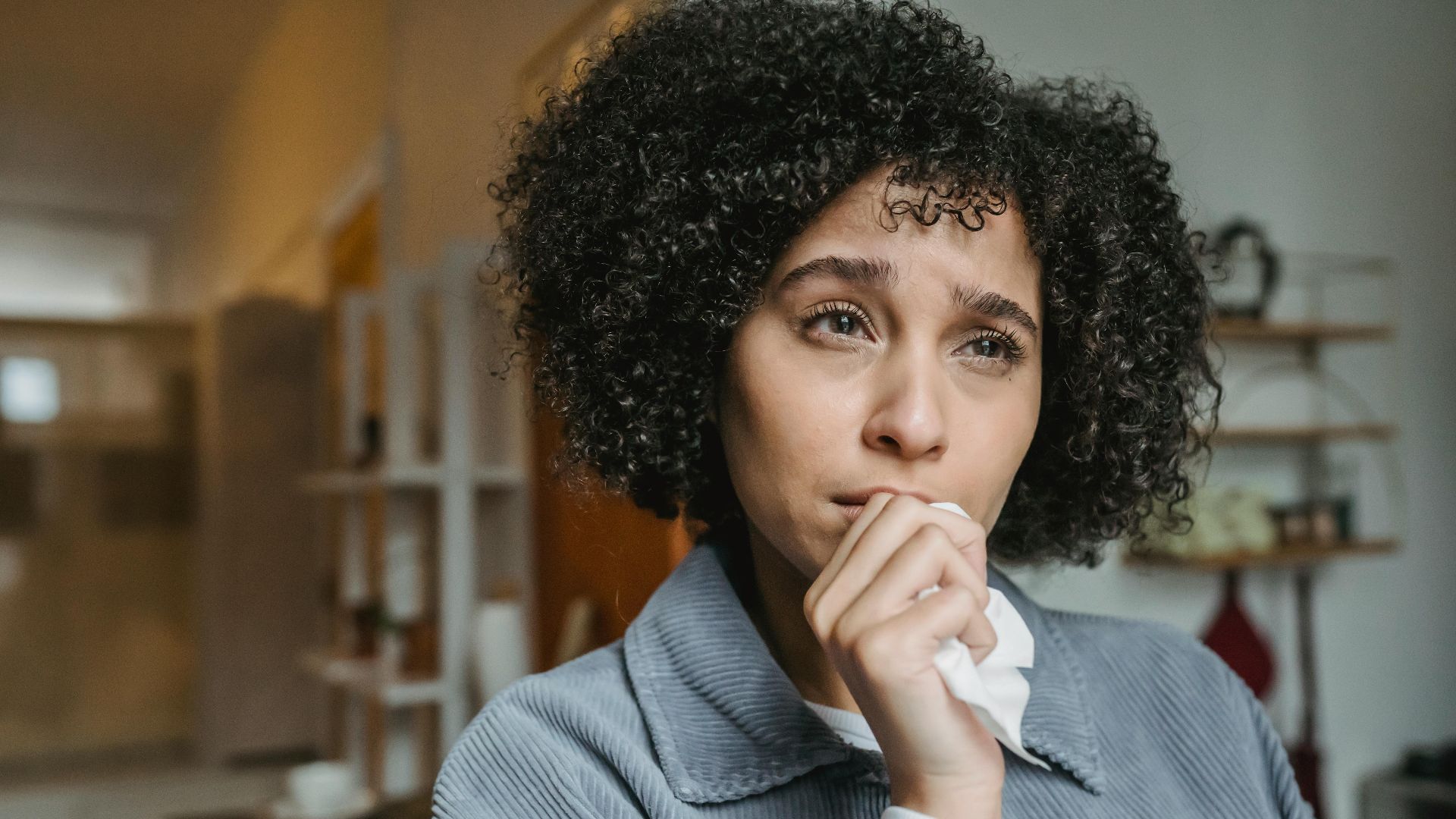 Unhappy African American woman with Afro hairstyle touching chin with tissue while looking away with sorrow