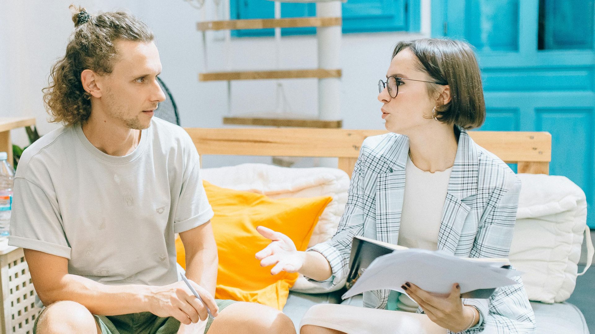 A man and woman discussing work in a stylish, bright living room setting.