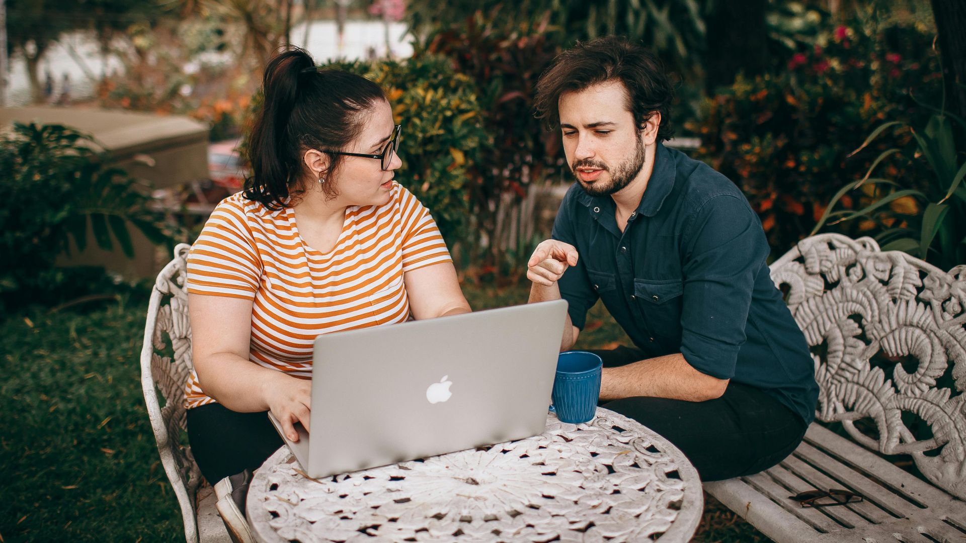 A man and woman working together on a laptop outdoors in a lush garden.