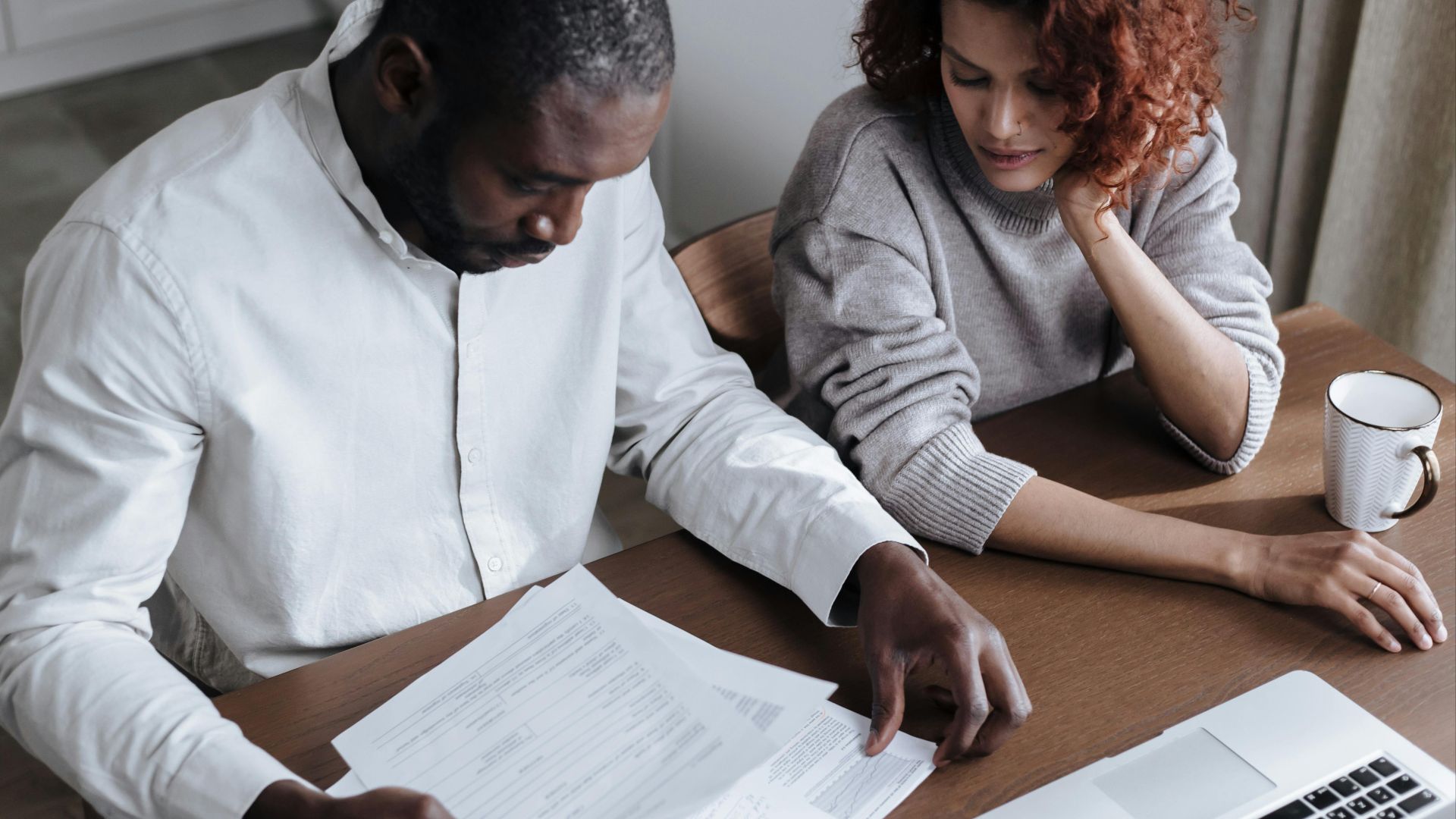 A couple reviews important documents together at a home desk with a laptop.