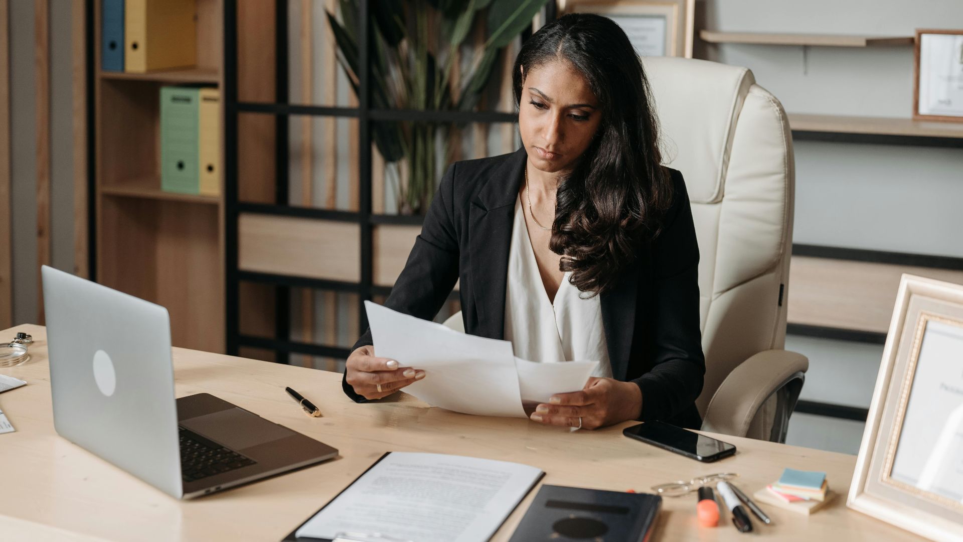 Business woman focused on paperwork at office desk, reviewing documents.