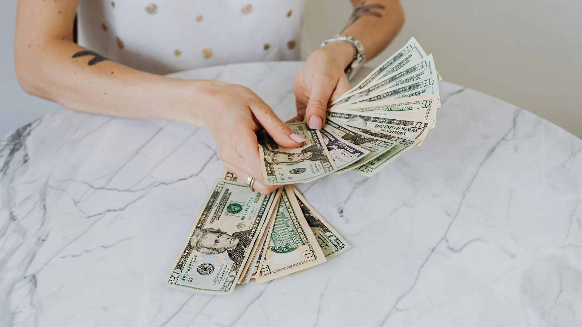 Close-up of a person counting US dollar bills on a luxurious marble table, symbolizing wealth and finance.