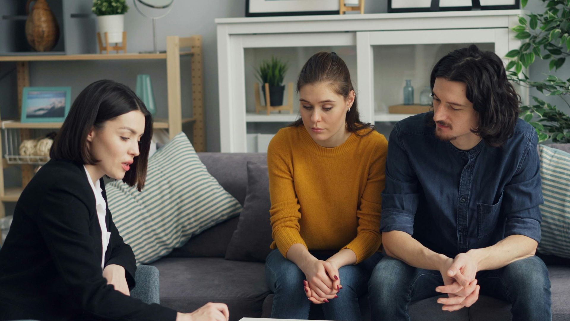 Couple discussing property with real estate agent in cozy living room setting, reviewing documents.
