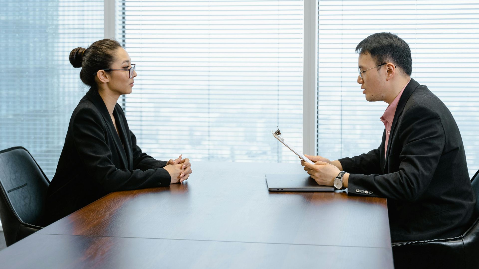 Two professionals in a business meeting in a modern office, facing each other across a table.