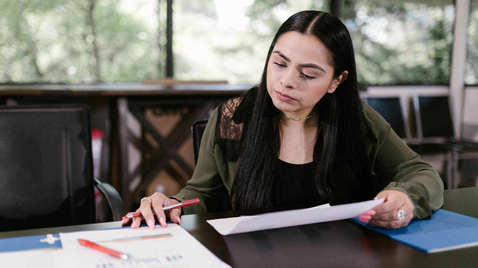 Professional woman in office setting studying documents with concentration.