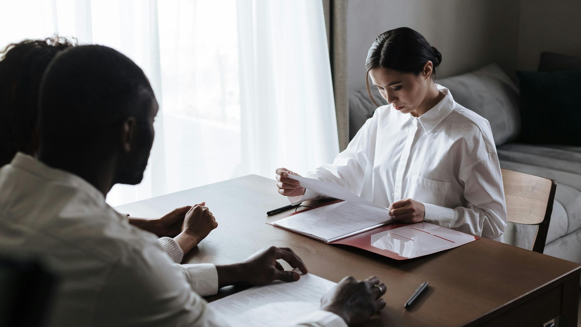 A professional woman reviews documents with a couple at home, indicating a collaborative decision-making process.