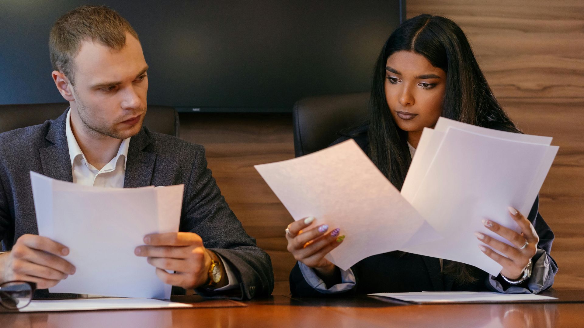 Two diverse professionals reviewing documents in a modern office setting, showcasing teamwork and focus.