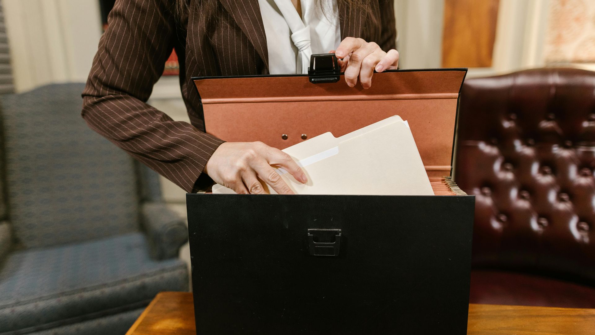 Close-up of a businesswoman organizing files in a black box in an office setting.