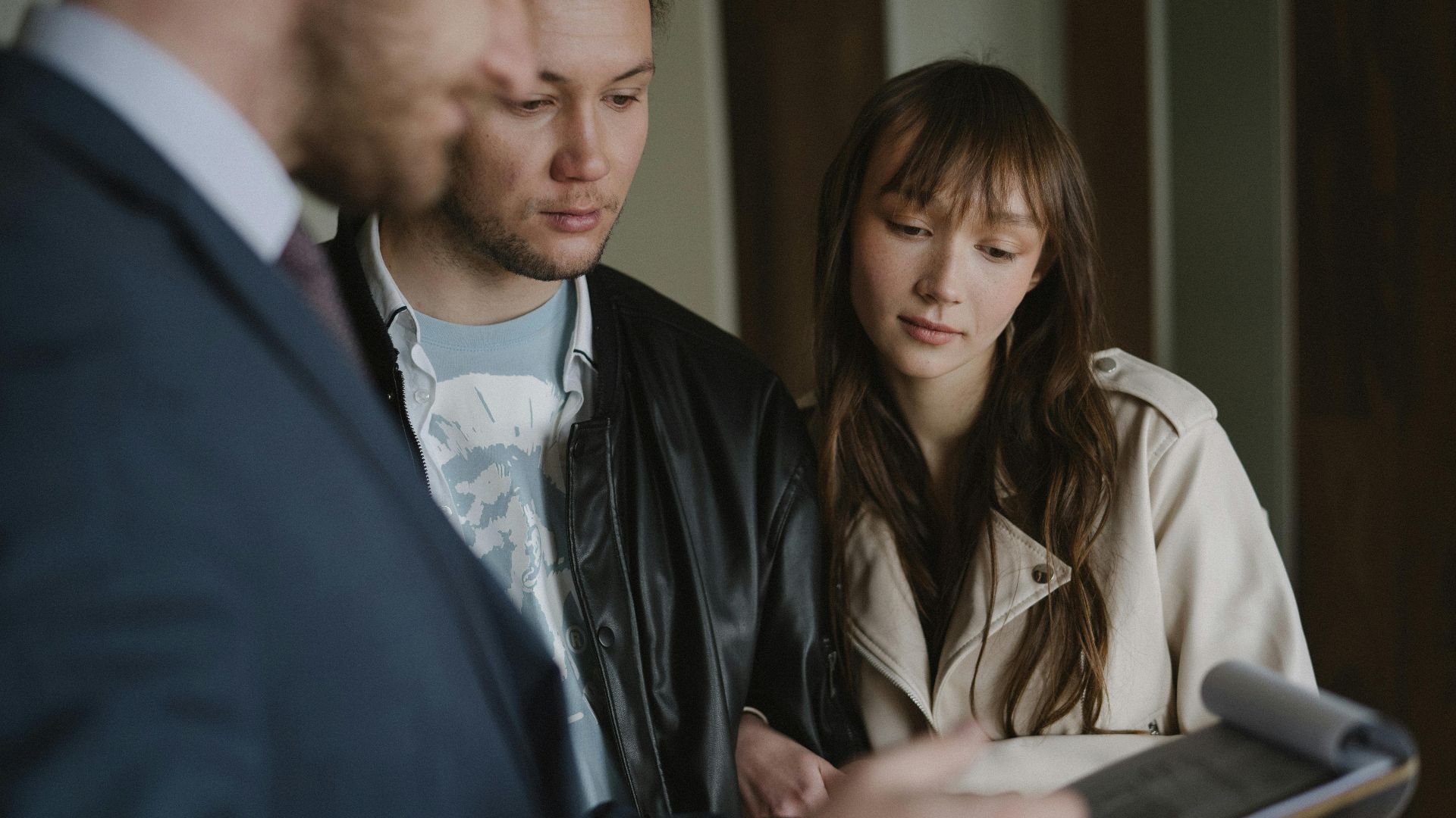 A couple discusses home buying details with a realtor inside a modern apartment.