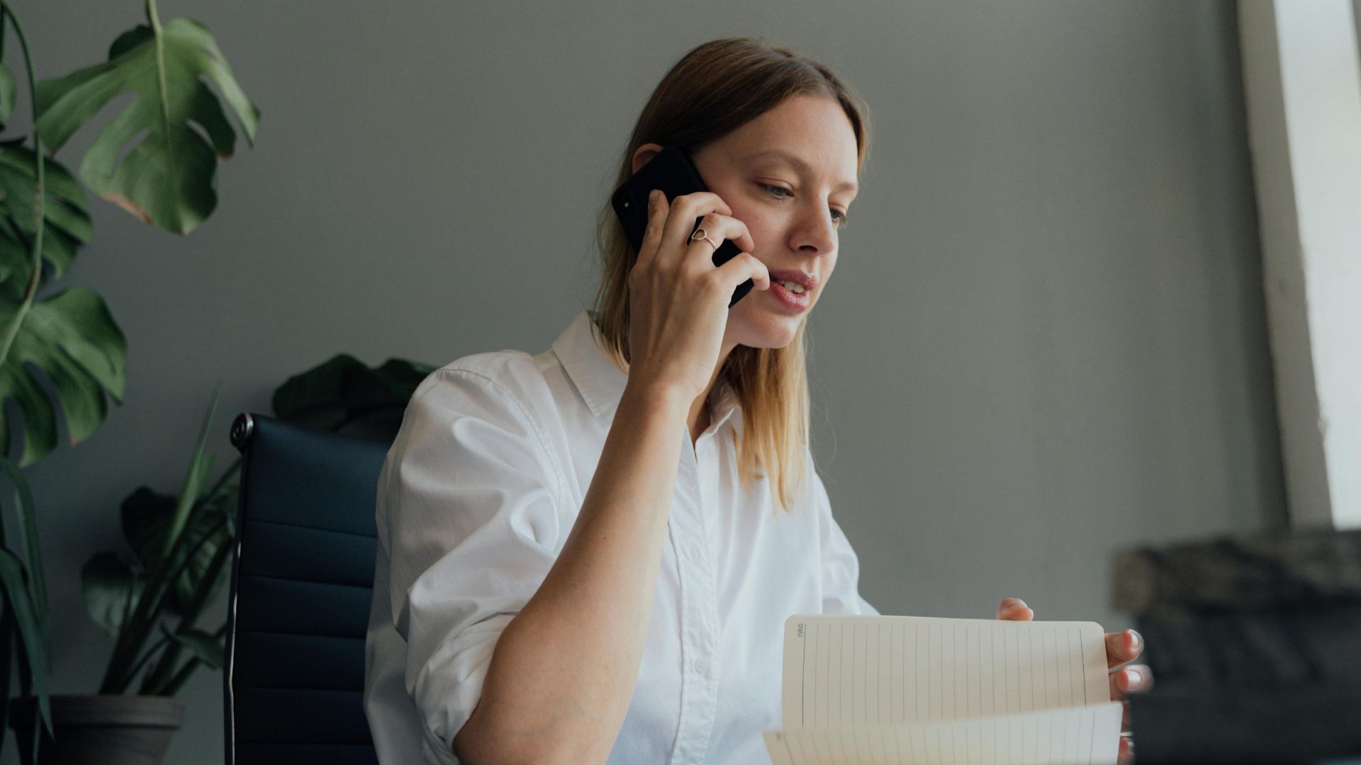 Woman on a phone call while reviewing documents at her desk indoors.