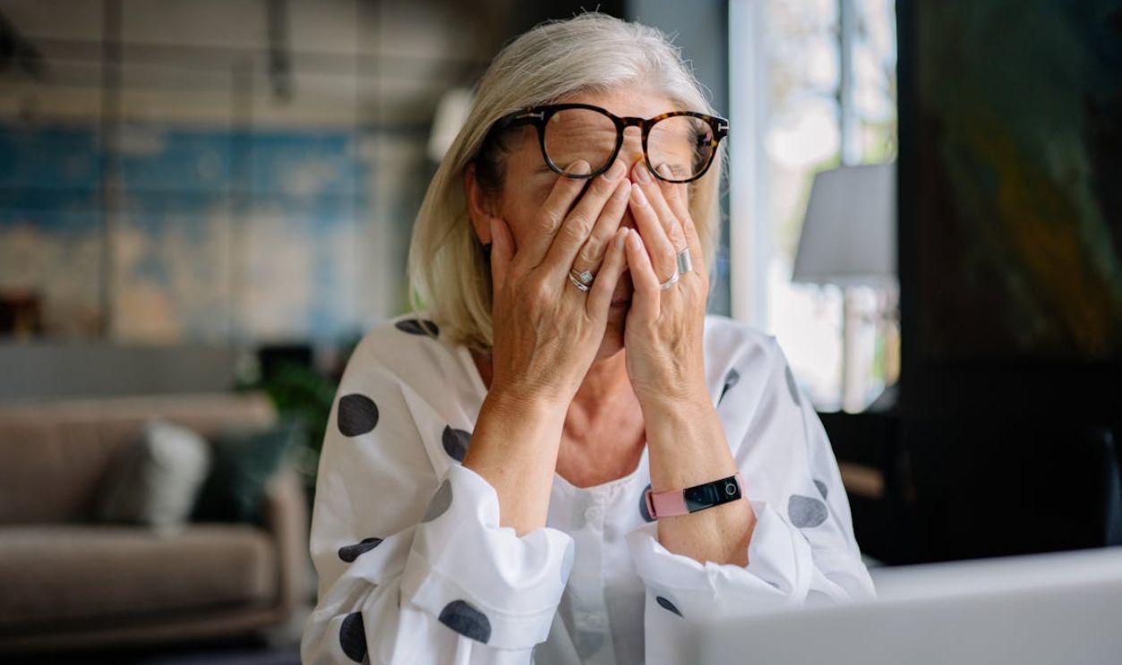 Senior woman experiencing stress indoors, covering face with hands. Reflects emotion and solitude