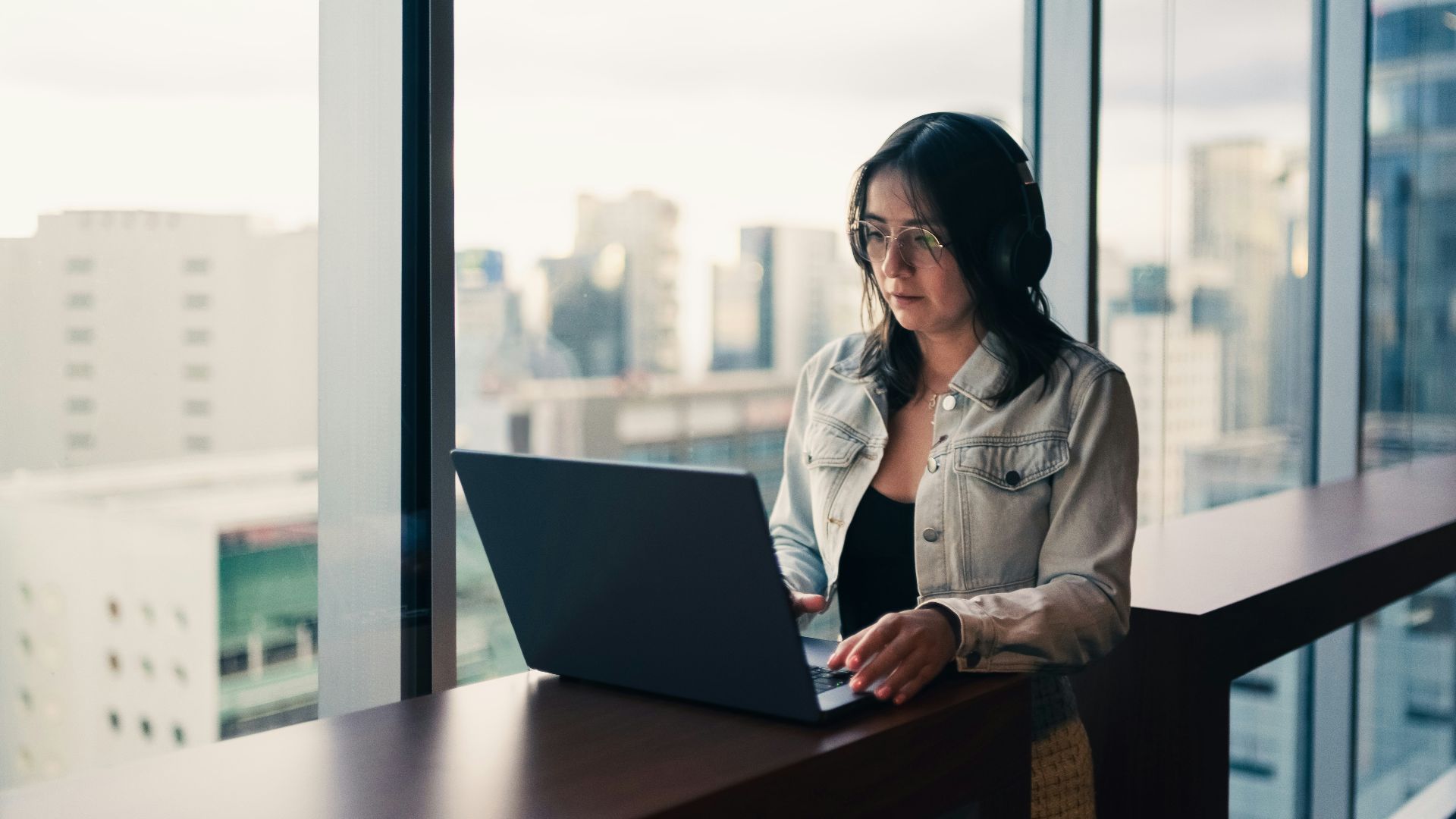 Woman wearing headphones working on a laptop by window