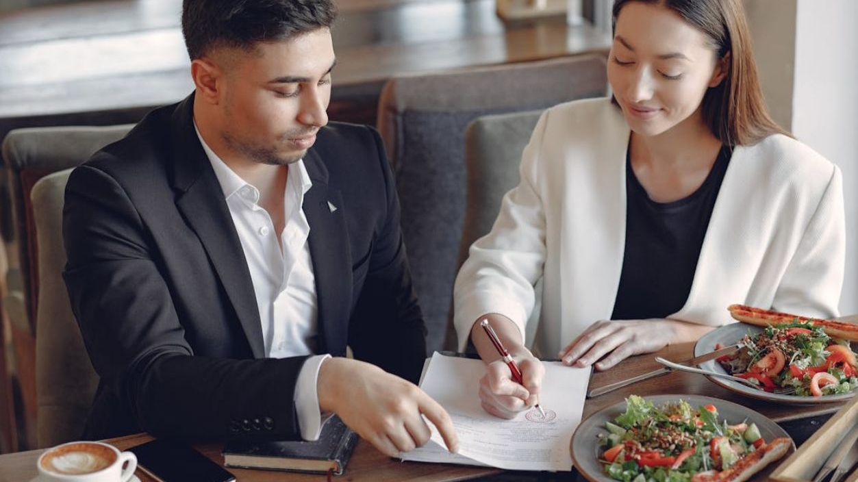 Content ethnic businesswoman signing contract while sitting with partner