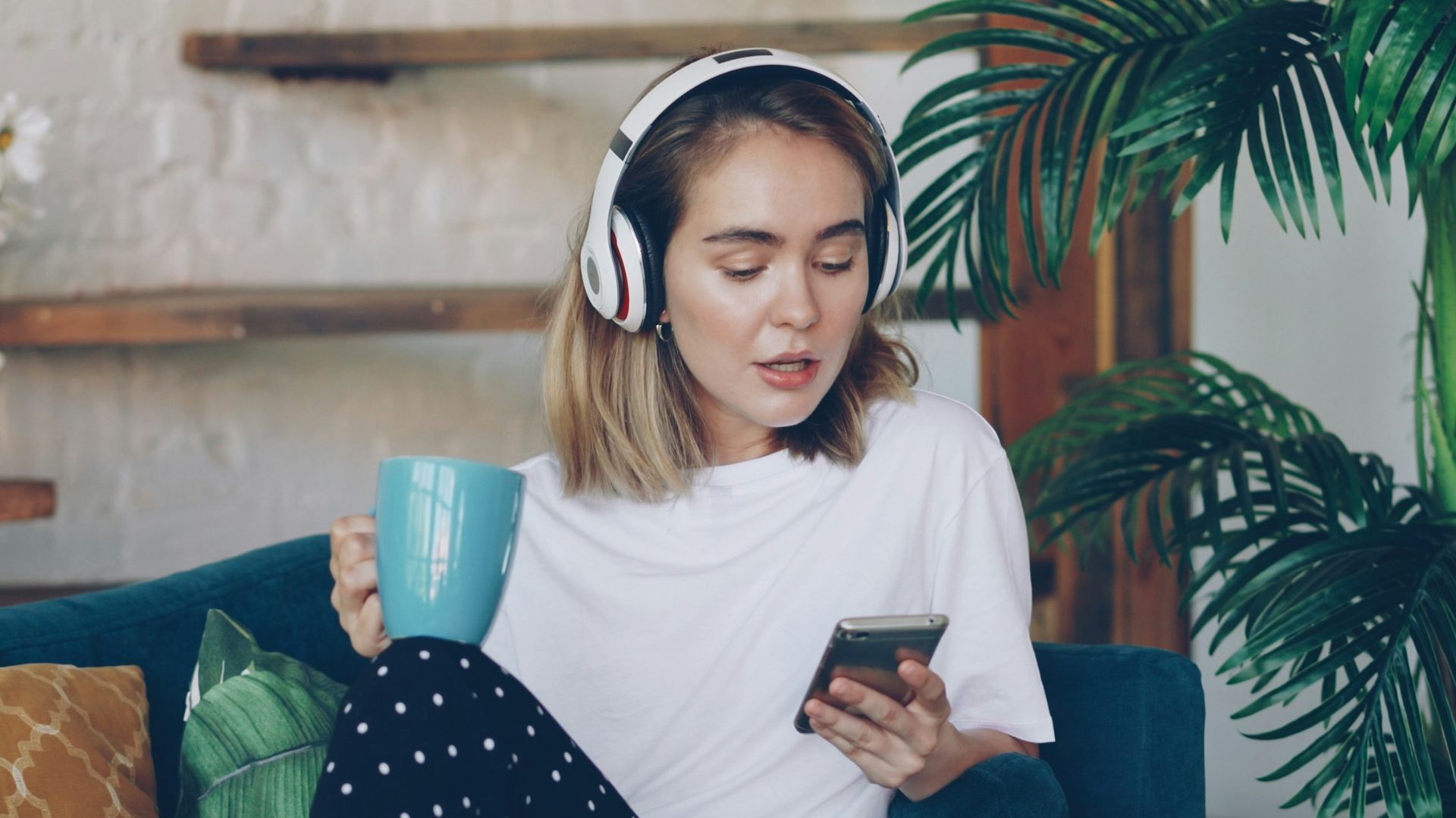 Woman listening to music on phone while holding mug.