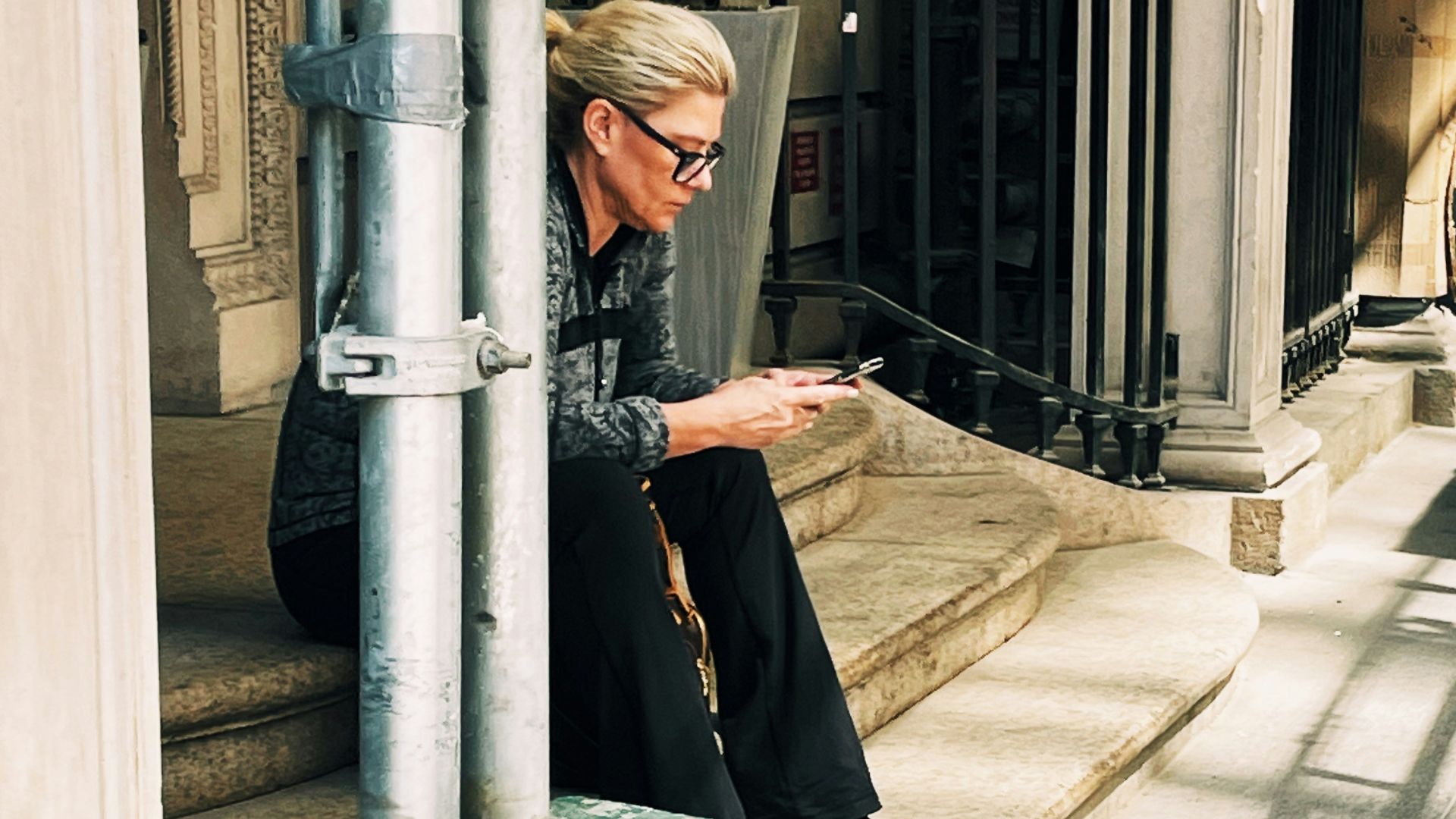 a woman sitting on the steps of a building looking at her cell phone