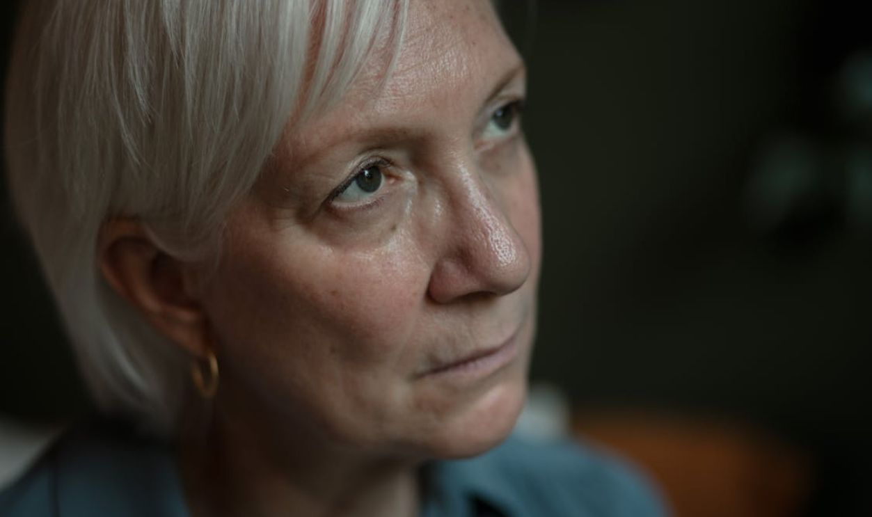 A close-up portrait of a thoughtful senior woman with white hair, indoors