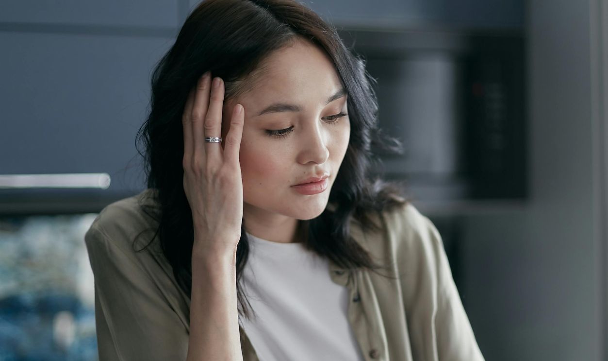A woman looks stressed while managing bills and documents at the kitchen table