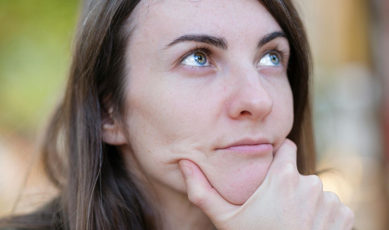 Close-up portrait of a woman thinking, with hand on chin, outdoors