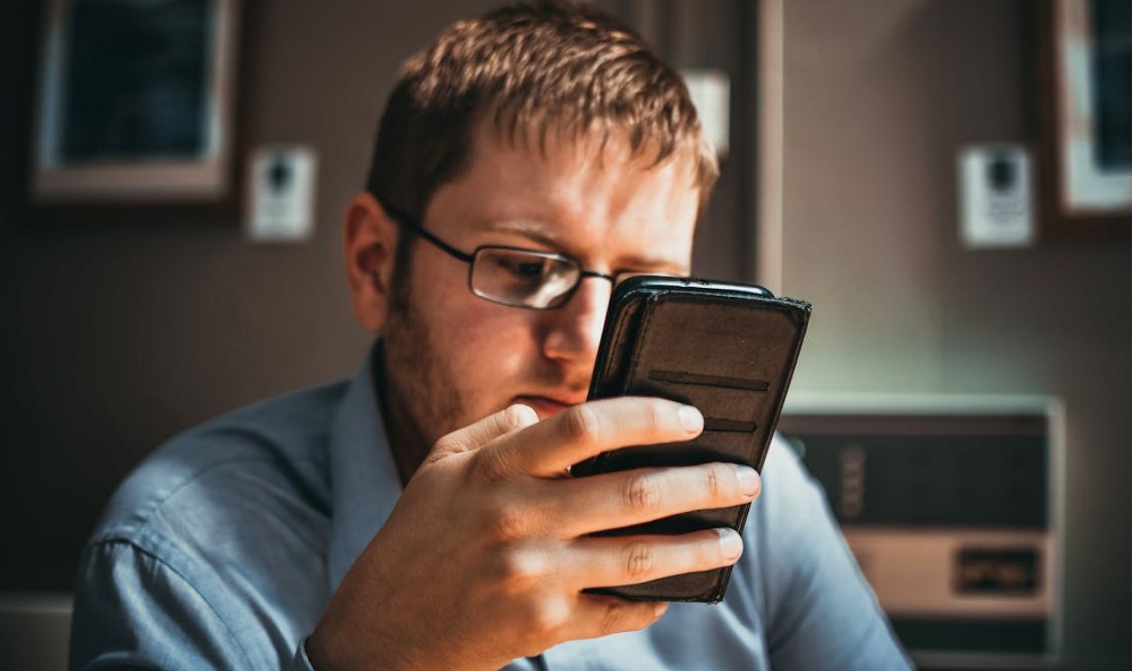 Serious businessman wearing glasses focused on smartphone in a modern office setting.