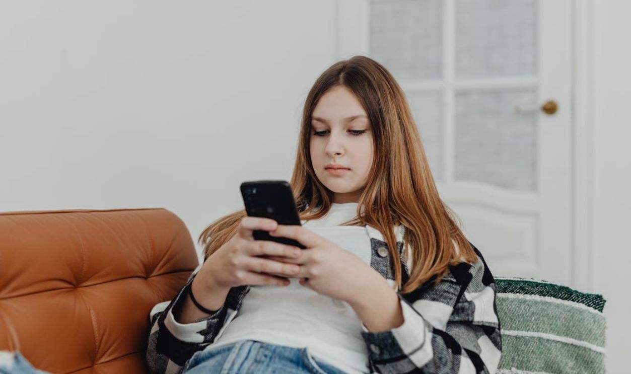 Teenage girl using smartphone while lounging on a sofa indoors.