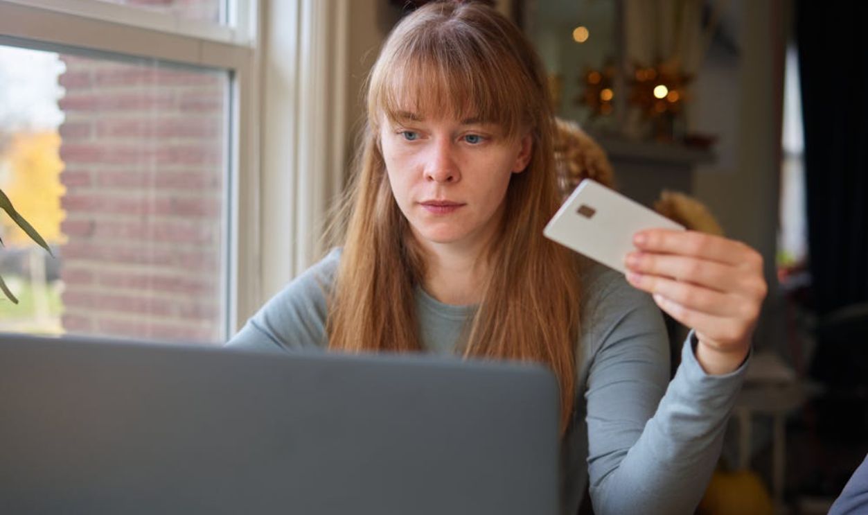 A young woman holds a credit card while using her laptop indoors.
