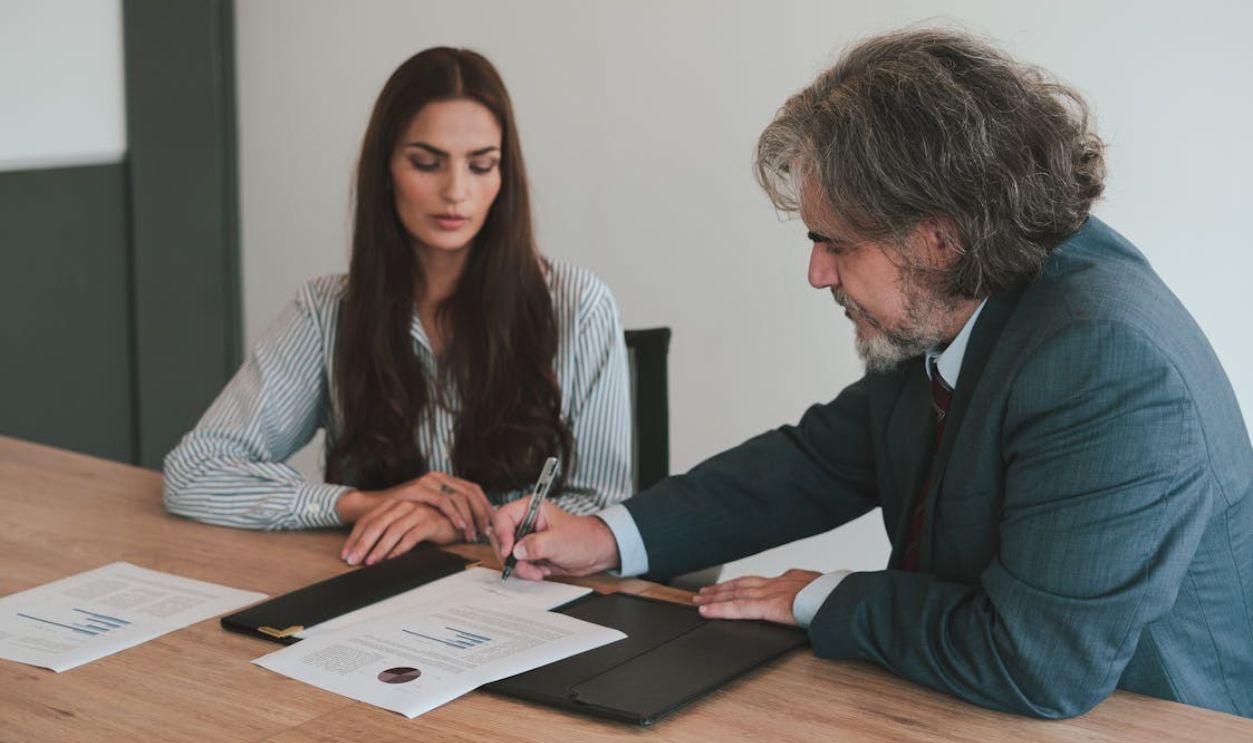Professional business meeting with two colleagues reviewing documents at an office desk.