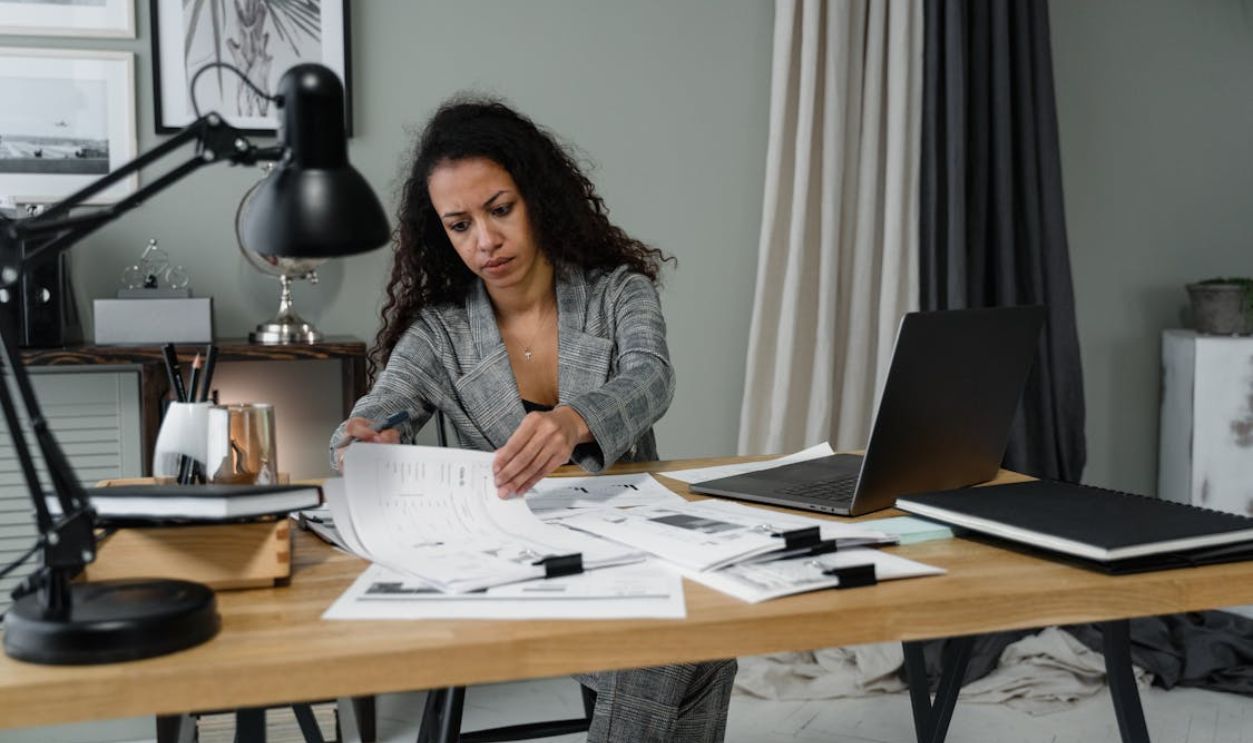 Businesswoman in office reviewing documents at desk with laptop and lamp.