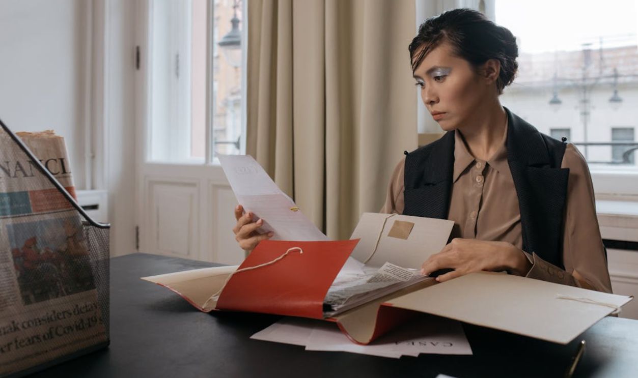 Businesswoman in an office setting reviewing important documents from a red folder with focus and determination.