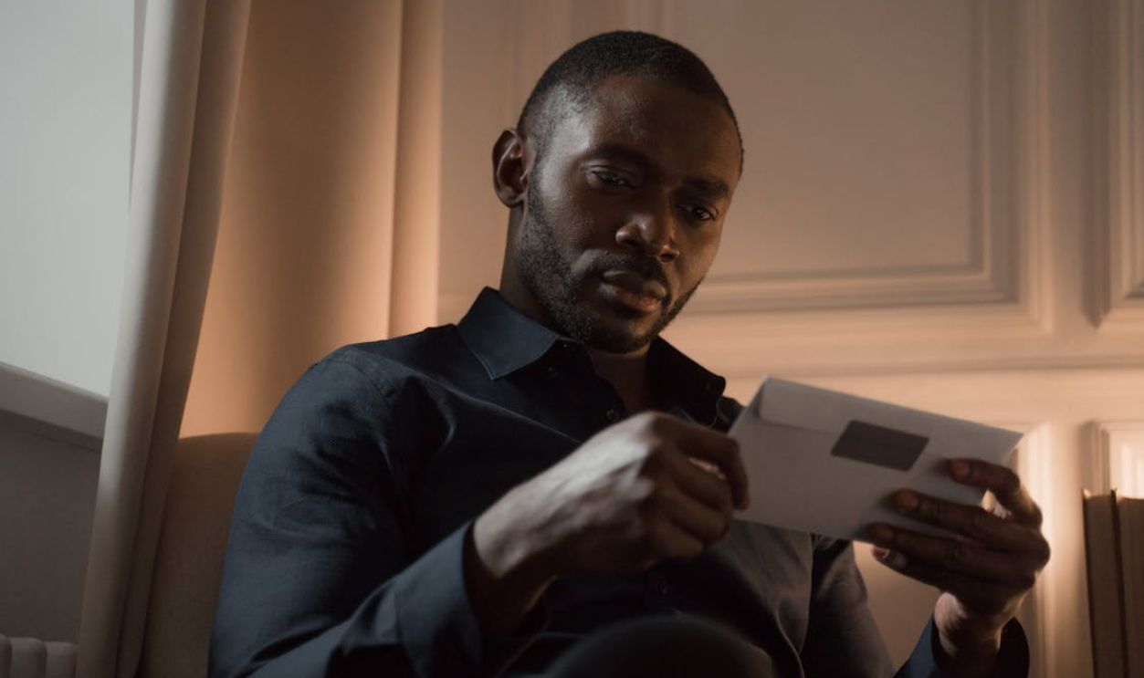 A man with a mustache reads a letter in a warmly lit room, creating a contemplative mood.