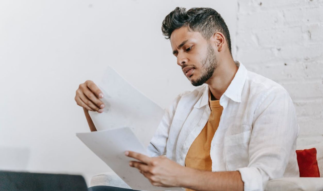A man in a white shirt sitting on a couch, deeply focused on reading documents.