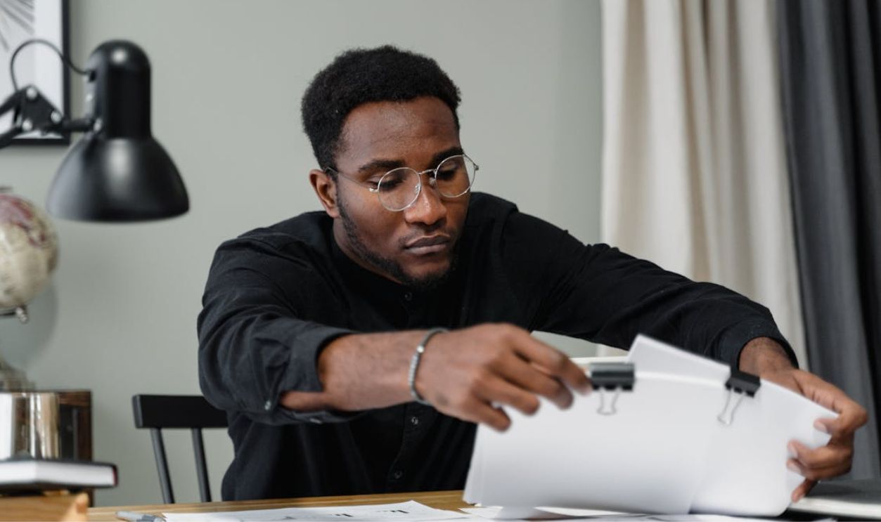 Professional man with glasses reviews documents at a desk in an office setting, emphasizing concentration.