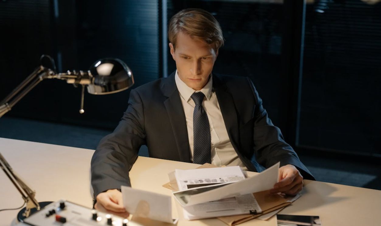 Focused investigator reviewing evidence in a dimly lit office setting.