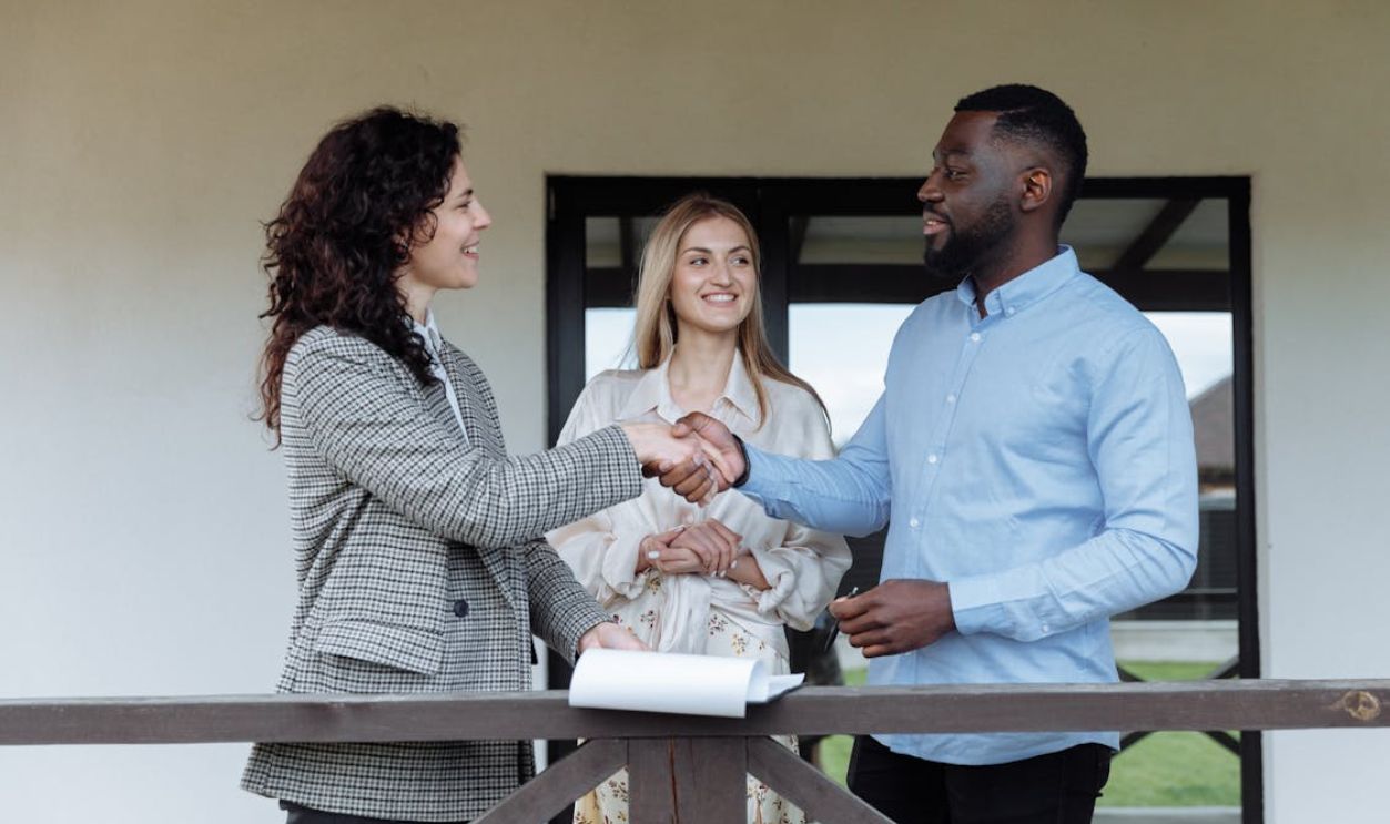 Three adults sealing a real estate deal with a handshake on a porch.
