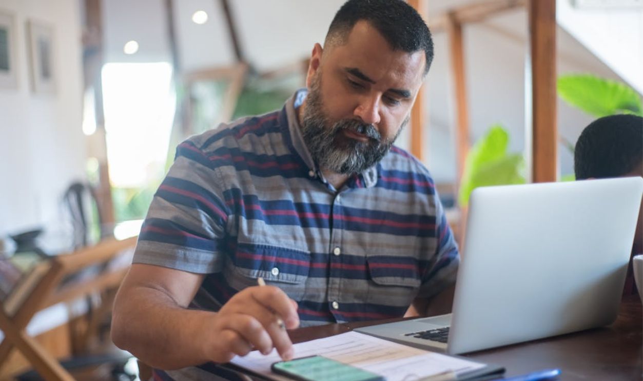 Professional man working at home office in Portugal using laptop and phone.