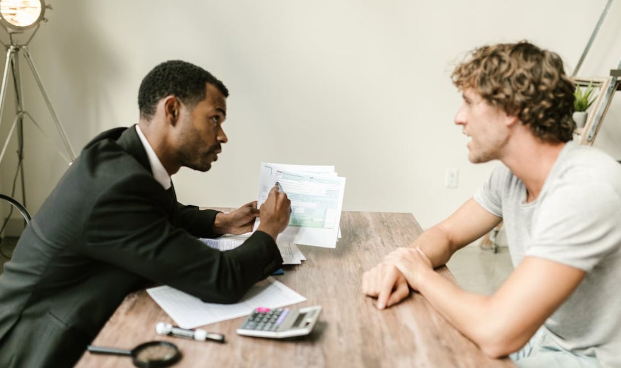 A financial advisor discusses paperwork with a client at a desk in a modern office.