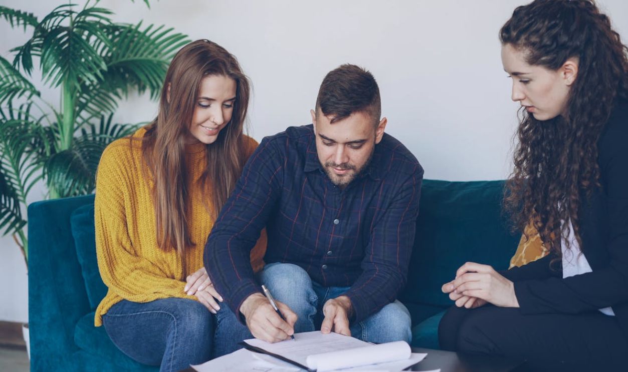 Young couple consults with financial advisor, signing important documents indoors.