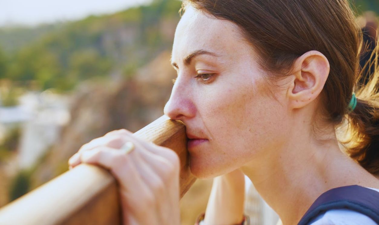 A thoughtful woman leans on a railing, lost in deep contemplation outdoors