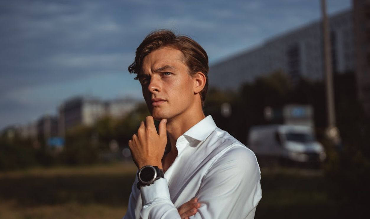 Portrait of a young man in white shirt outdoors, exuding a contemplative mood against an urban backdrop