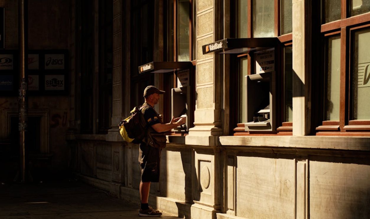 An adult male using an ATM on a historic street corner in warm sunset lighting