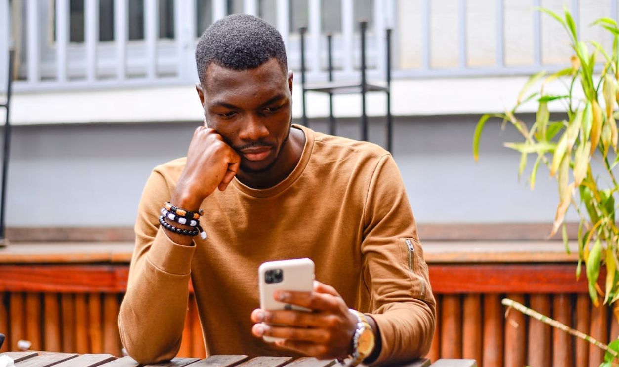 African American man sitting outside, using a smartphone, in thoughtful pose