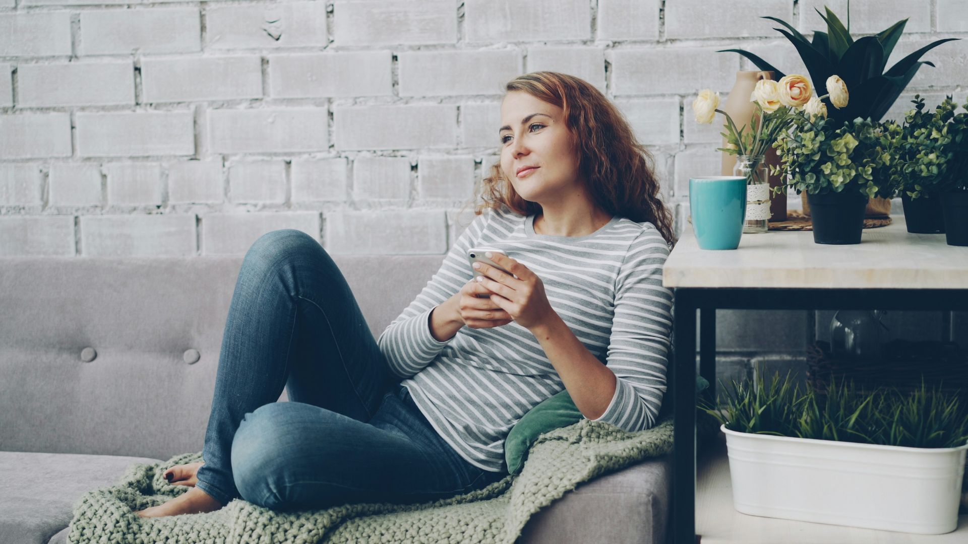 Woman relaxing on sofa with phone and coffee.