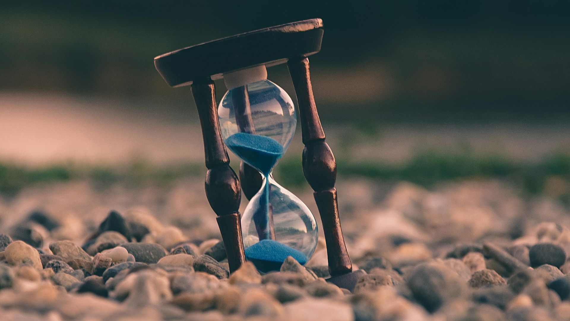 selective focus photo of brown and blue hourglass on stones