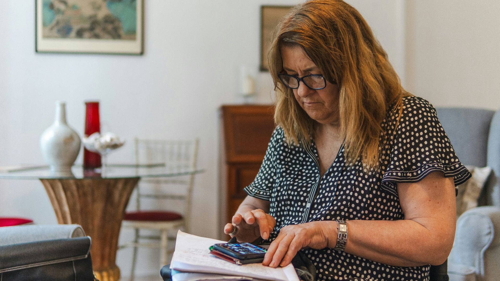 Woman using calculator with papers on table.