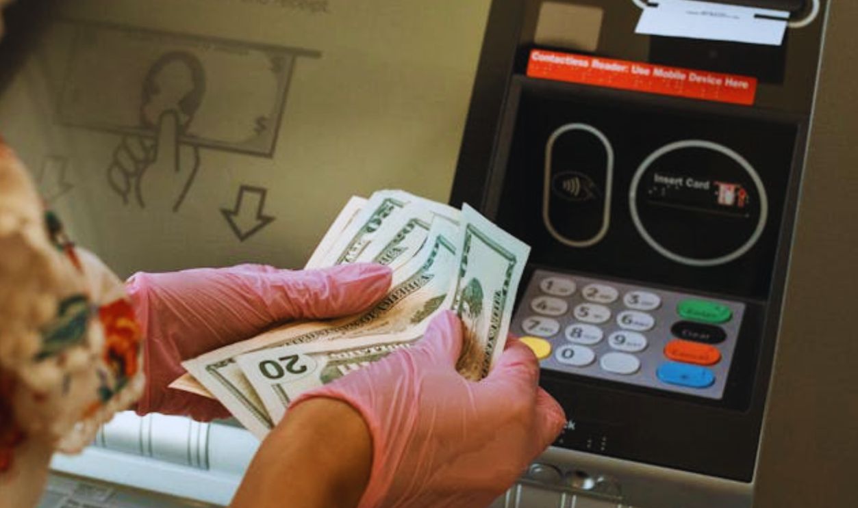 A person wearing gloves withdraws cash from an ATM, ensuring hygiene