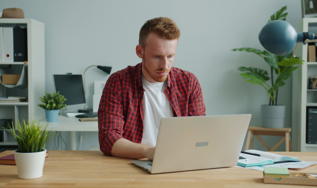 Focused young man in casual attire working on laptop in stylish home office.